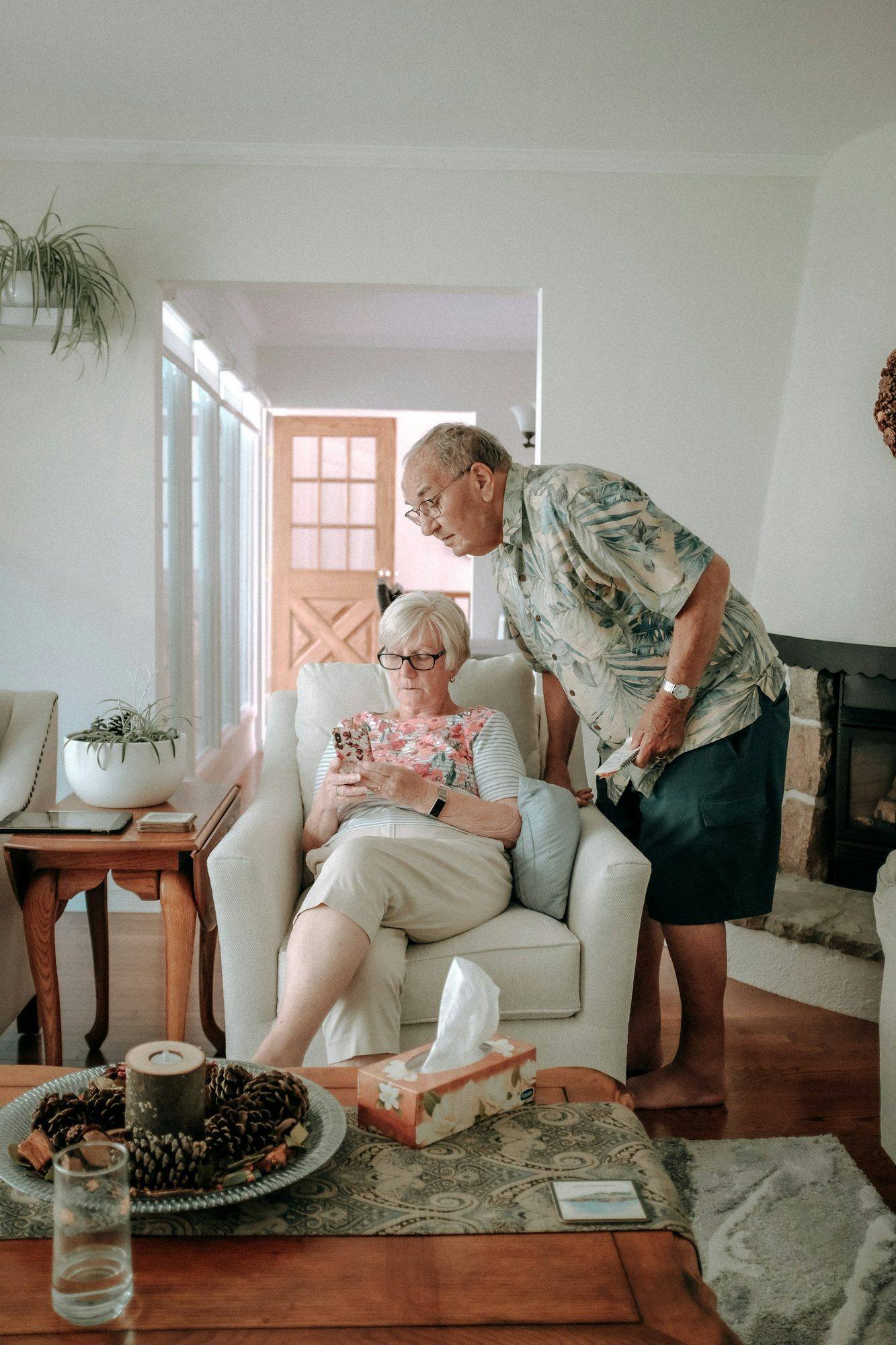 A man checking on an older woman sitting in an armchair in her living room
