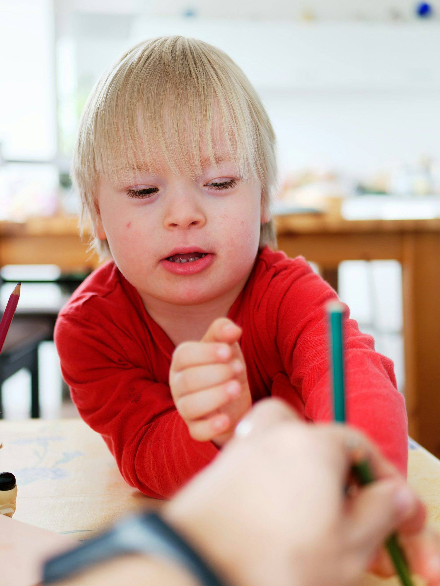 A young boy drawing at a table while an adult helps