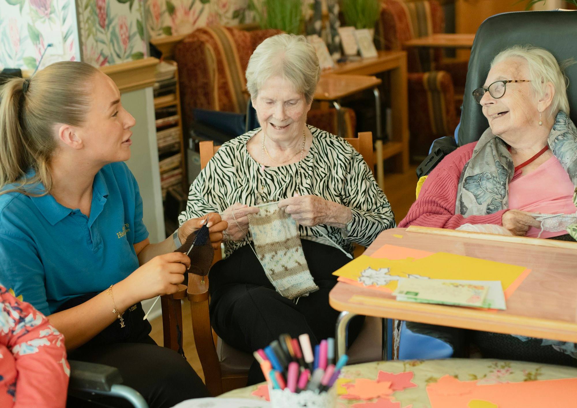 A caregiver knitting with two older women at a table