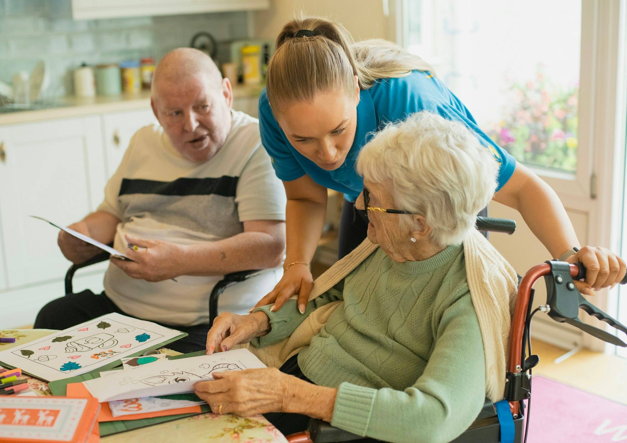 A caregiver helping an older man and woman with a colouring activity
