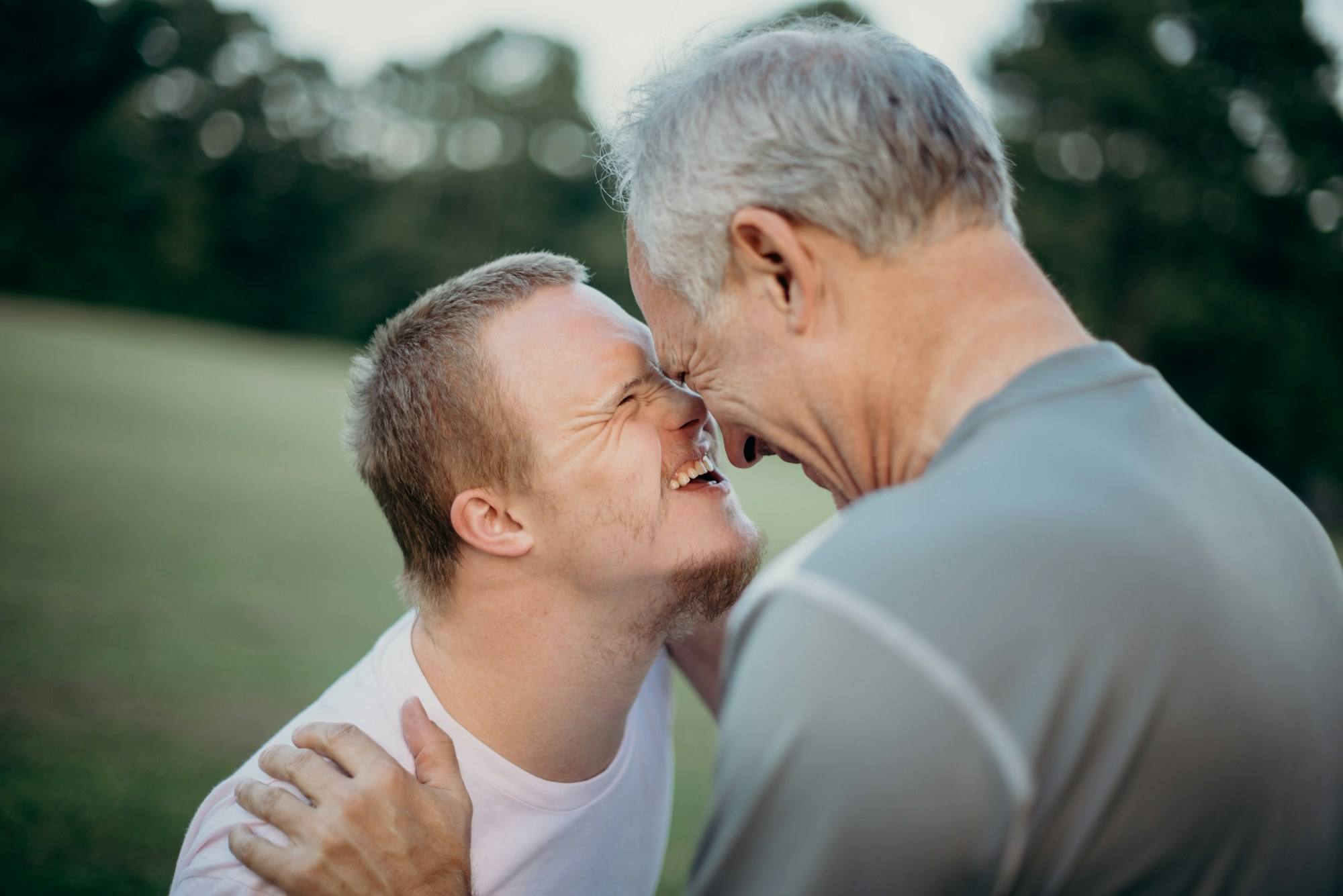 A young man with Down syndrome sharing a laugh with an older man outdoors