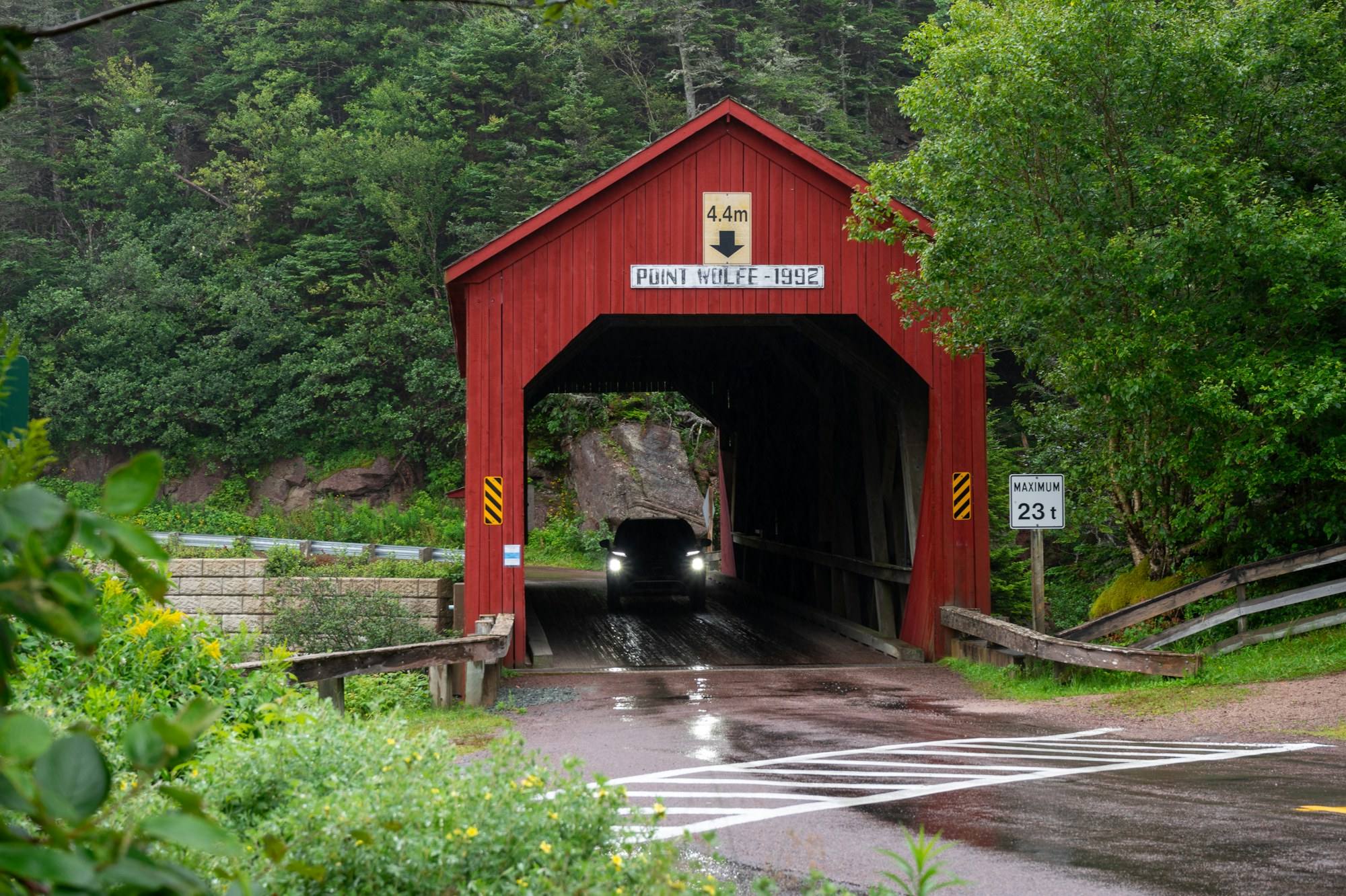 A red covered bridge on a green, wooded road in southern New Brunswick
