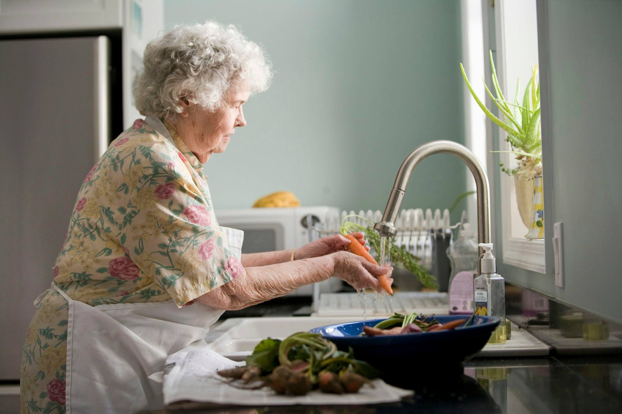 An older woman washing vegetables at her kitchen sink