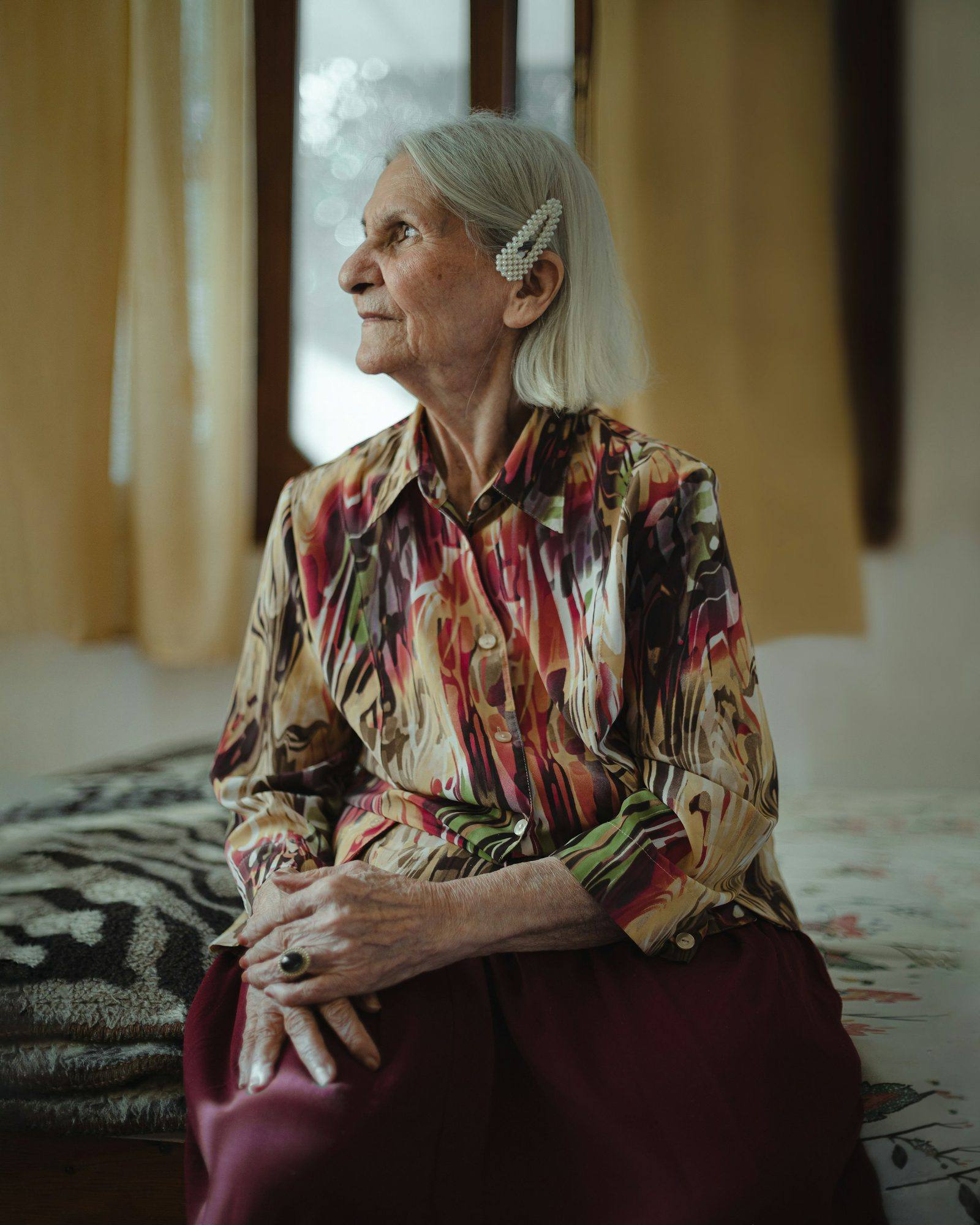 An older woman sitting on the edge of her bed in a quiet bedroom