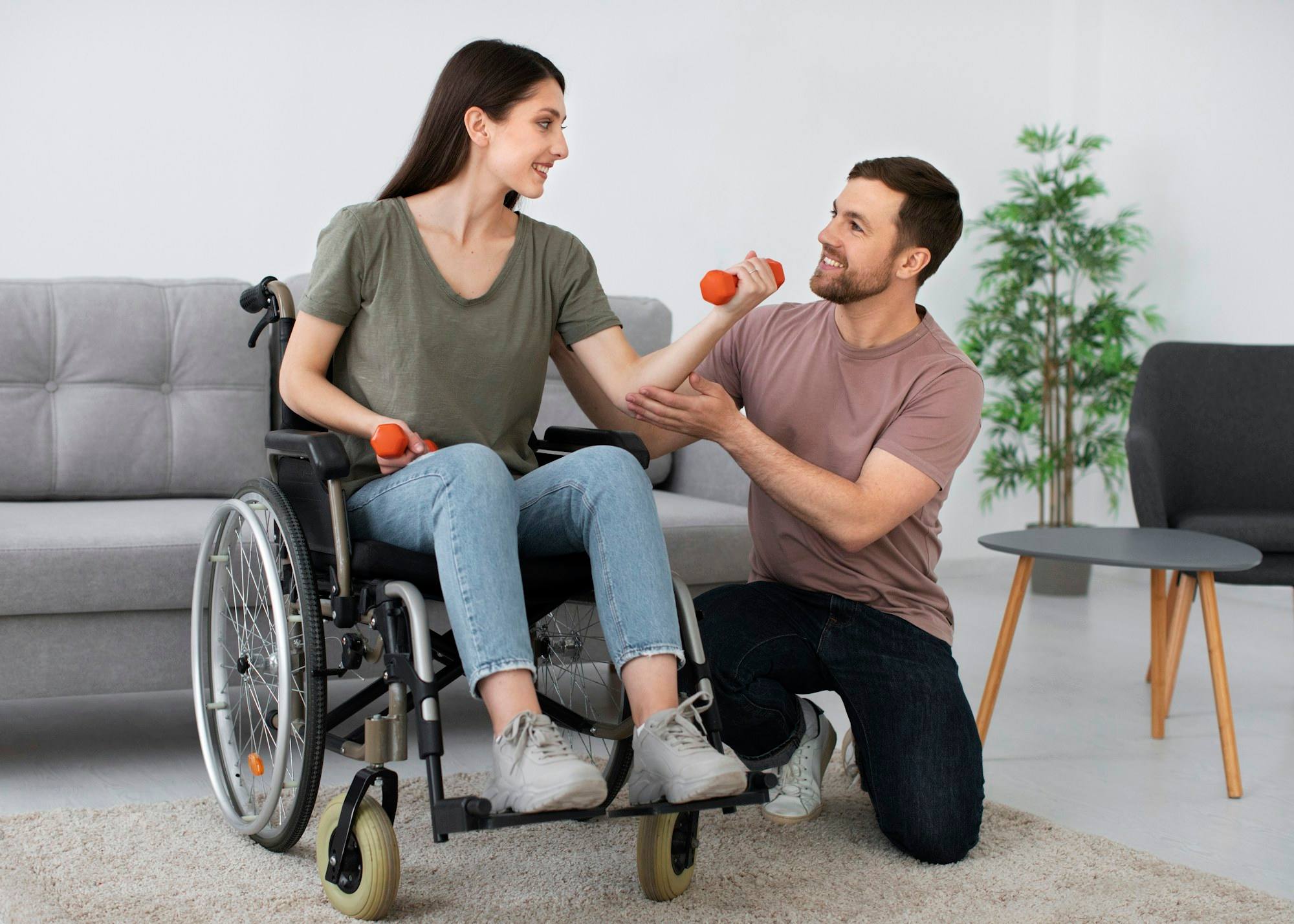A woman in a wheelchair doing arm exercises with a man kneeling beside her