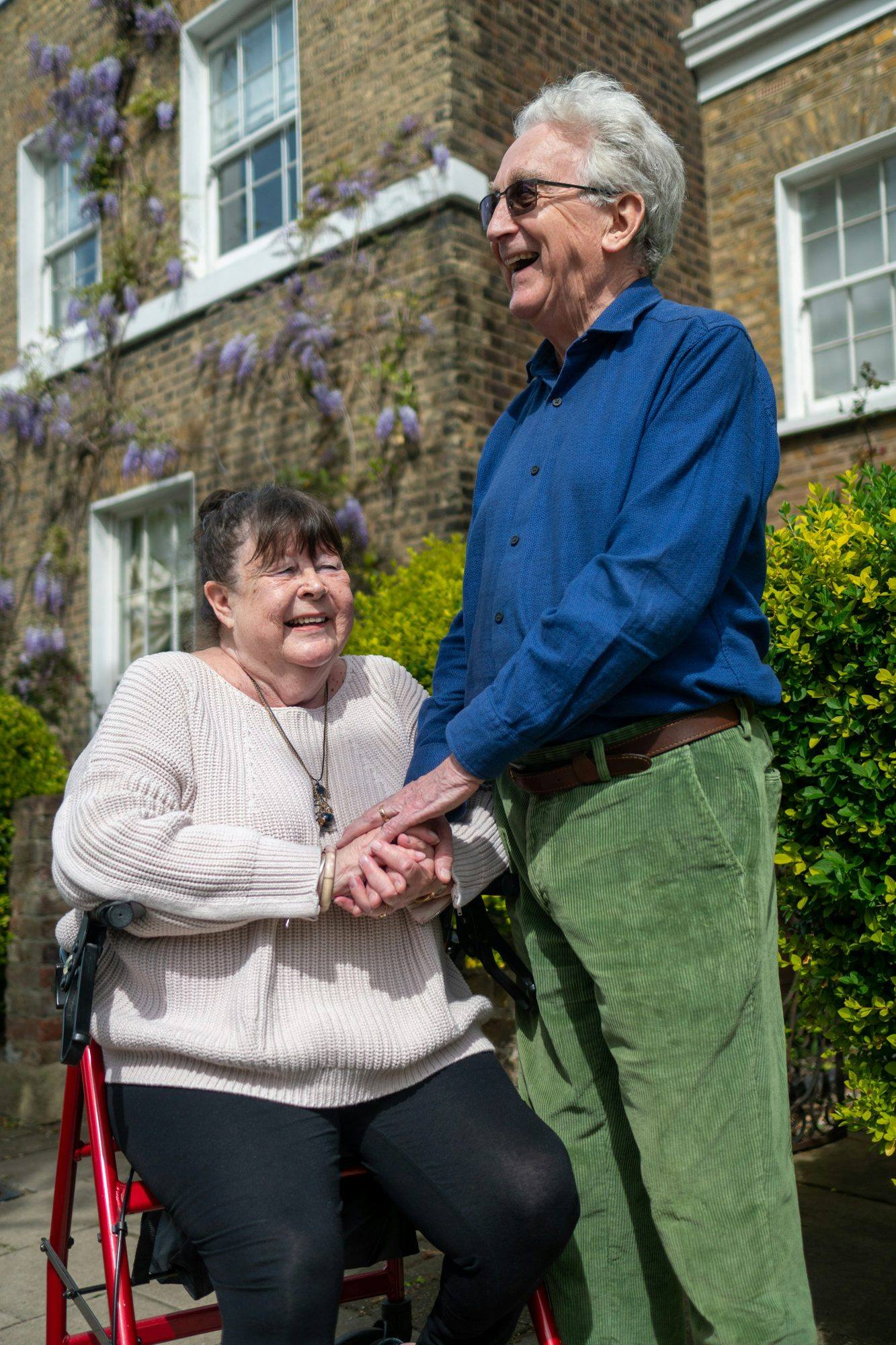 An older woman seated on her walker, holding hands with a man in a garden